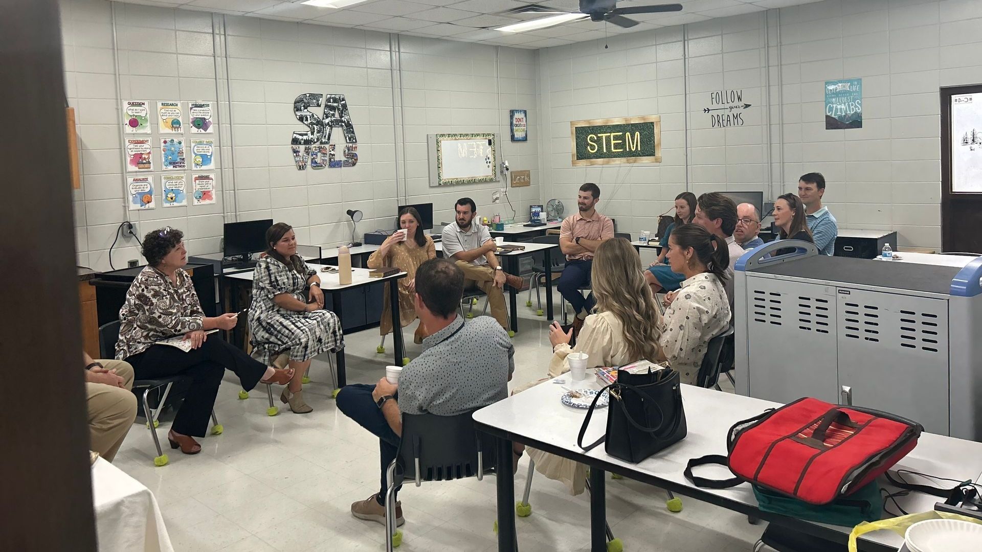 A group of people are sitting around tables in a classroom.