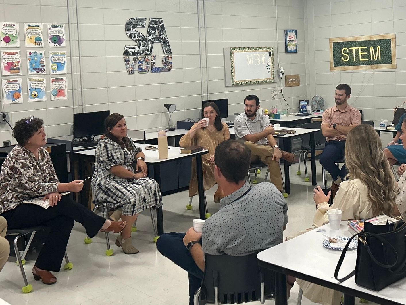 A group of people are sitting around tables in a classroom.