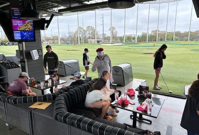 A group of people are sitting at tables in front of a golf course.