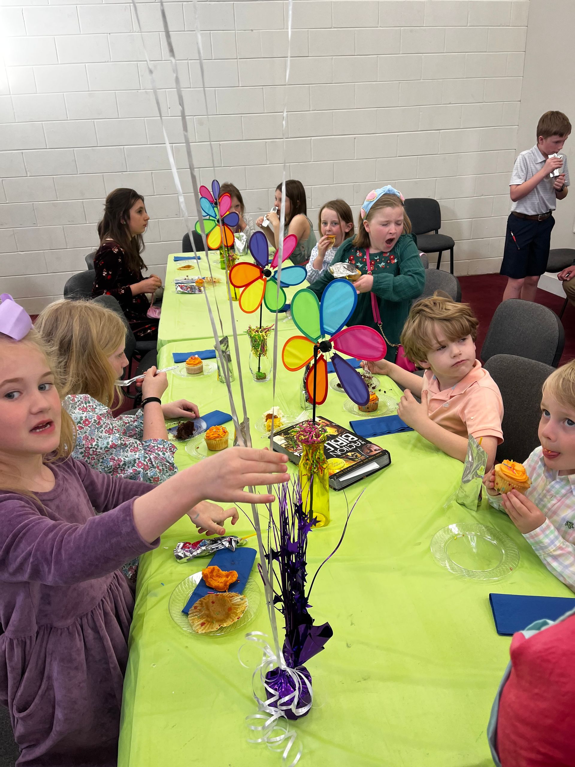 A group of children are sitting at a long table eating food.