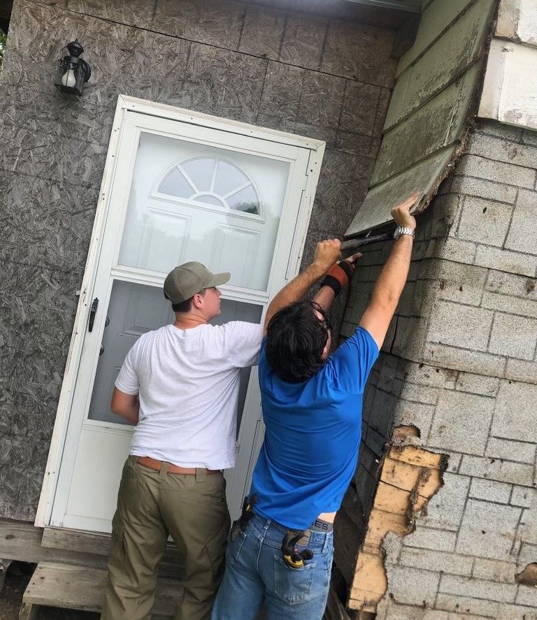 Two men are working on a door on a brick building.