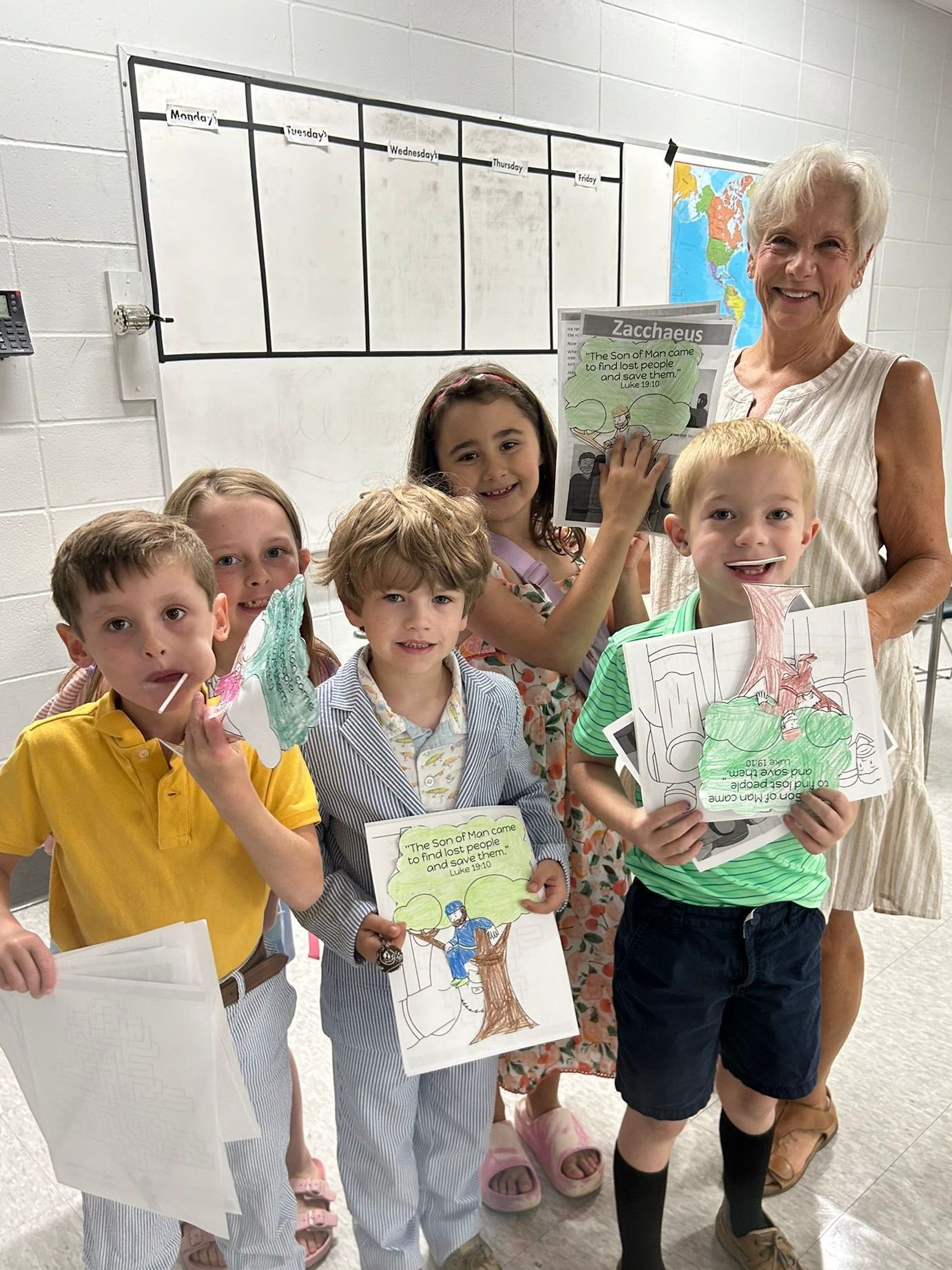 A group of children are standing next to each other in a classroom holding drawings.