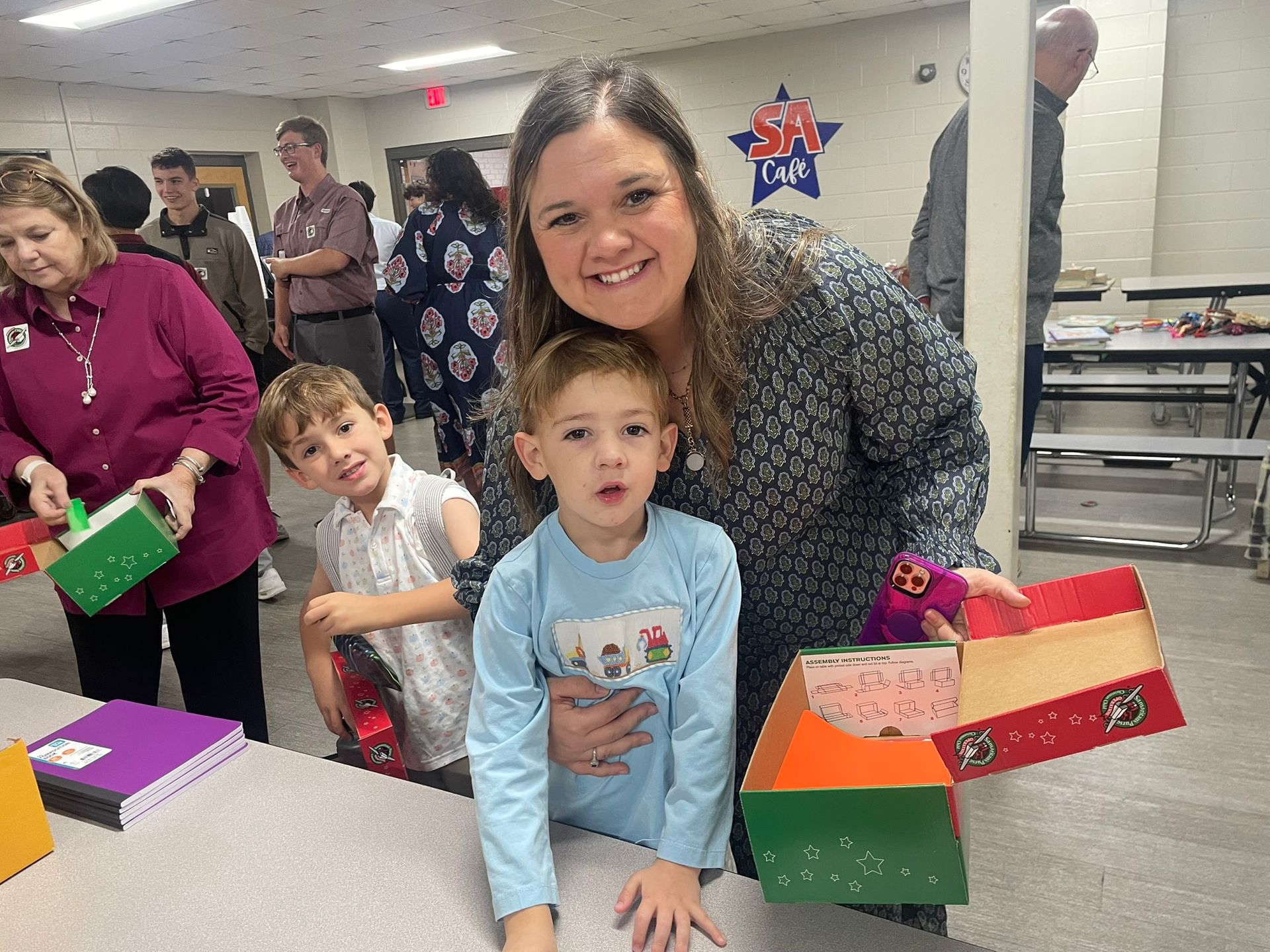 Woman and two children pose with colorful handmade boxes in a room with other adults.