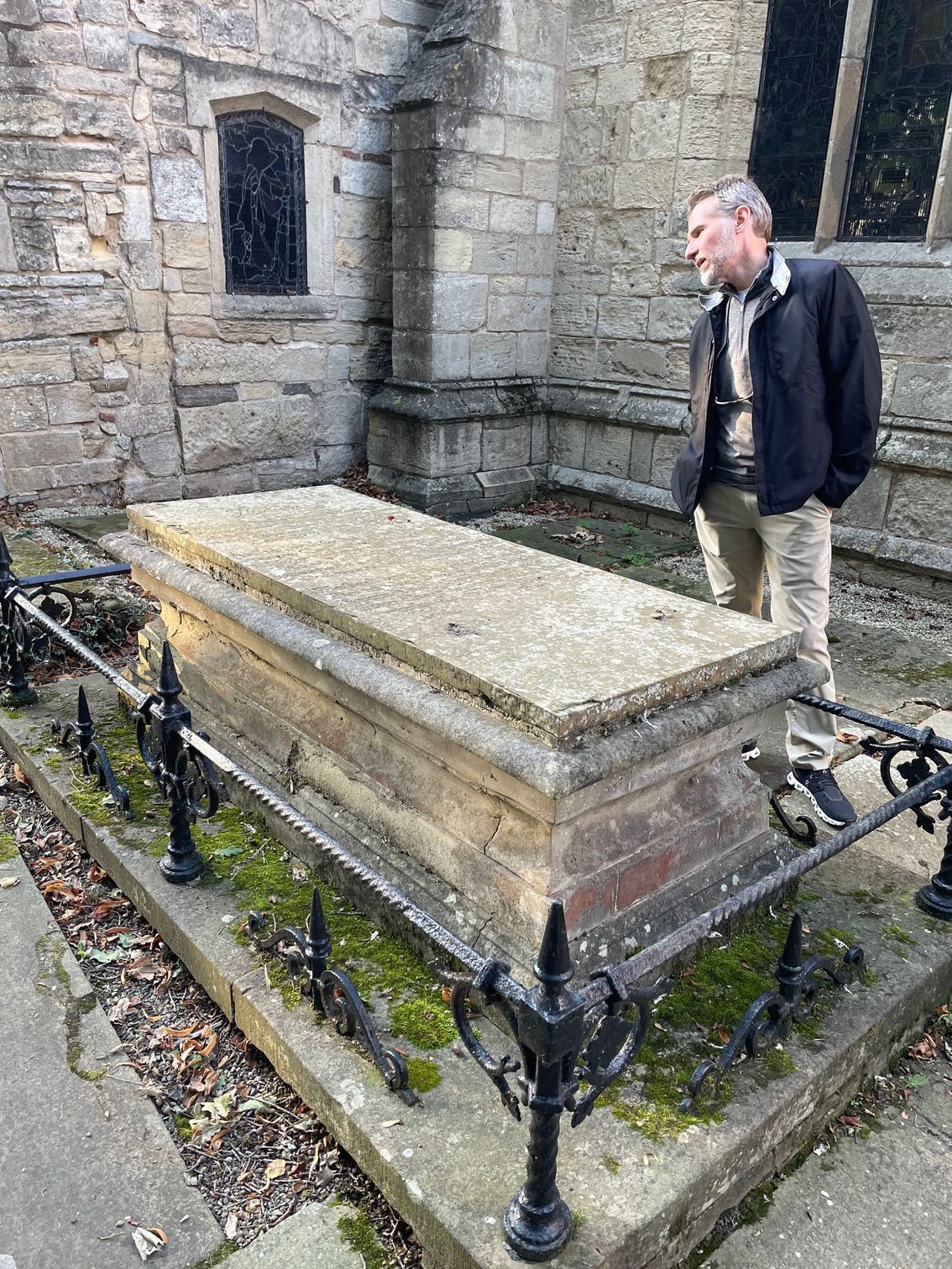 Man standing beside a stone tomb with a wrought iron fence, next to a church.