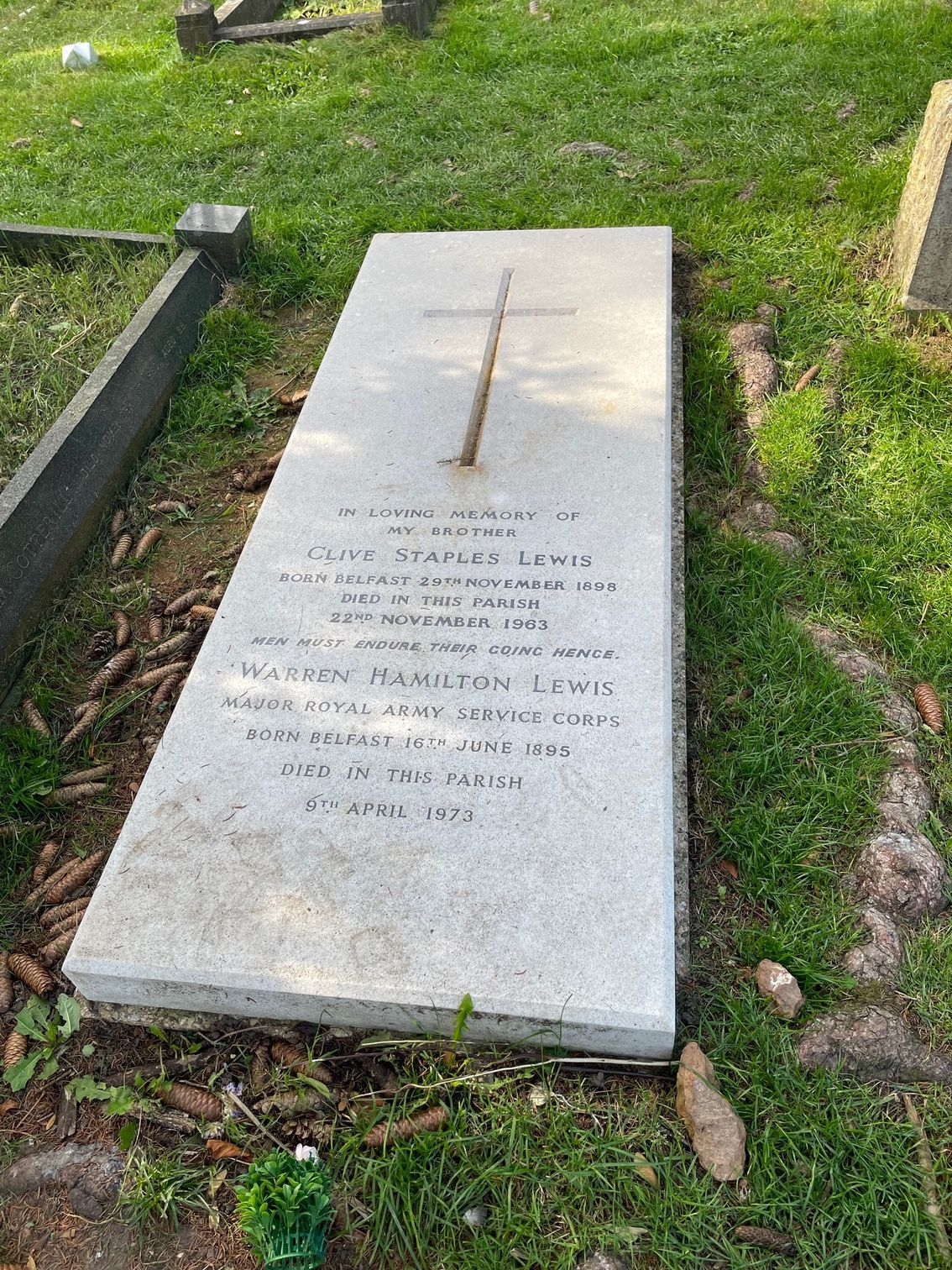 A rectangular, stone gravestone with a cross etched on it; text is carved on its surface, lying on grass.