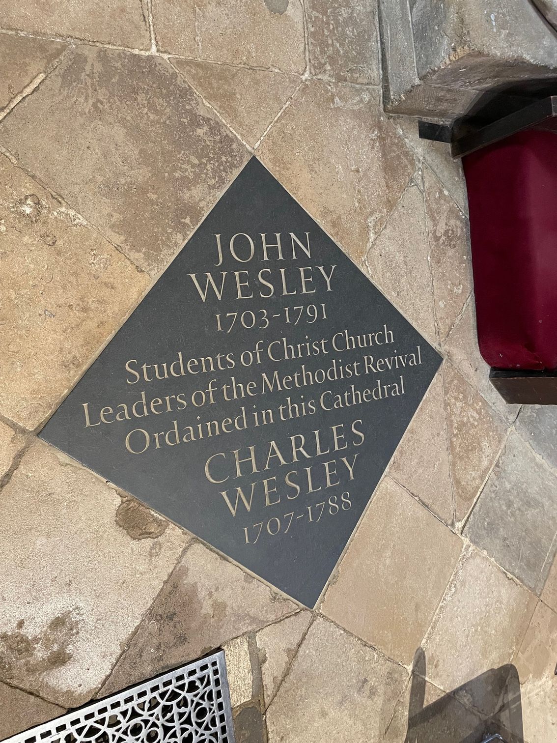 Black stone plaque in a diamond shape, names John and Charles Wesley. Embedded in a cobblestone surface.