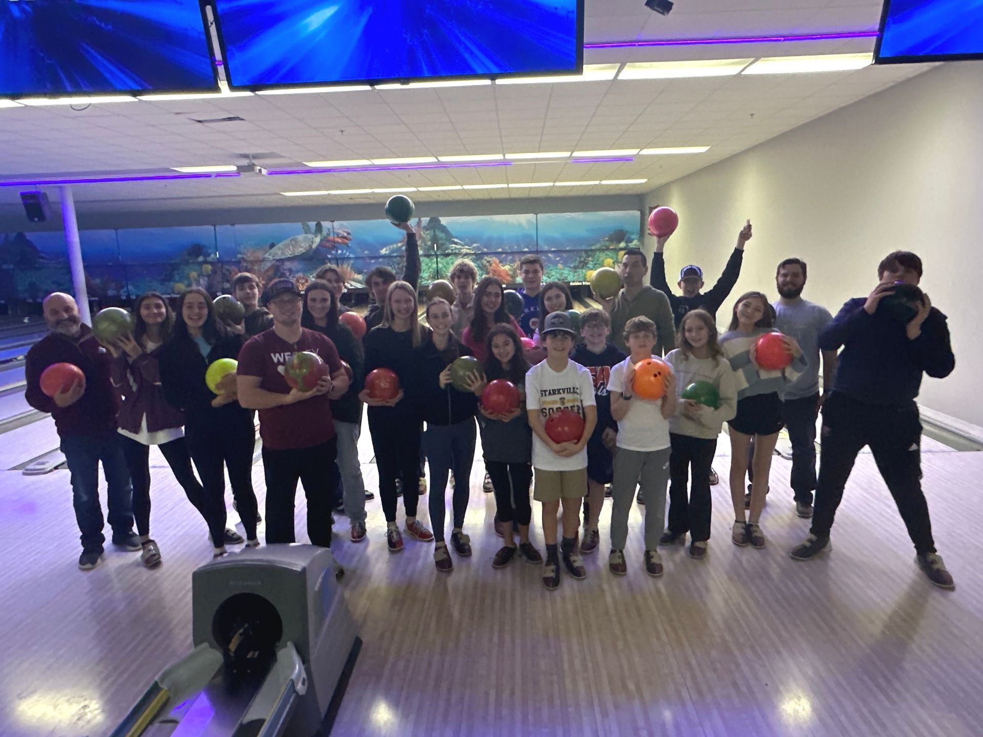 A group of people are standing in a bowling alley holding bowling balls.
