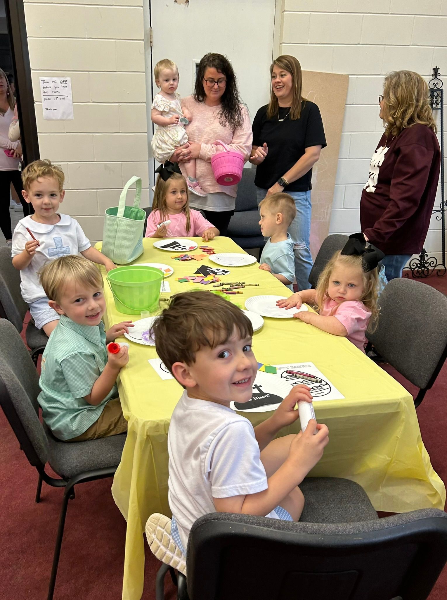 A group of children are sitting at a table with a yellow table cloth.