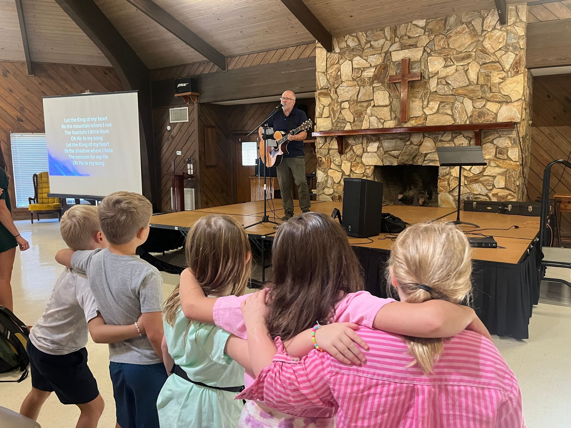 A man is playing a guitar in front of a group of children.