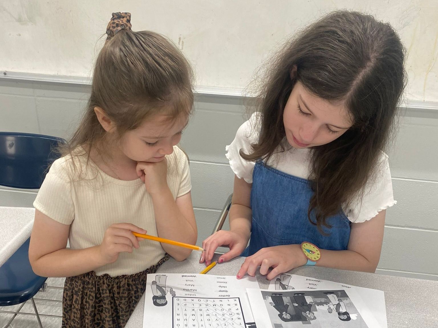 Two young girls are sitting at a table looking at a piece of paper.