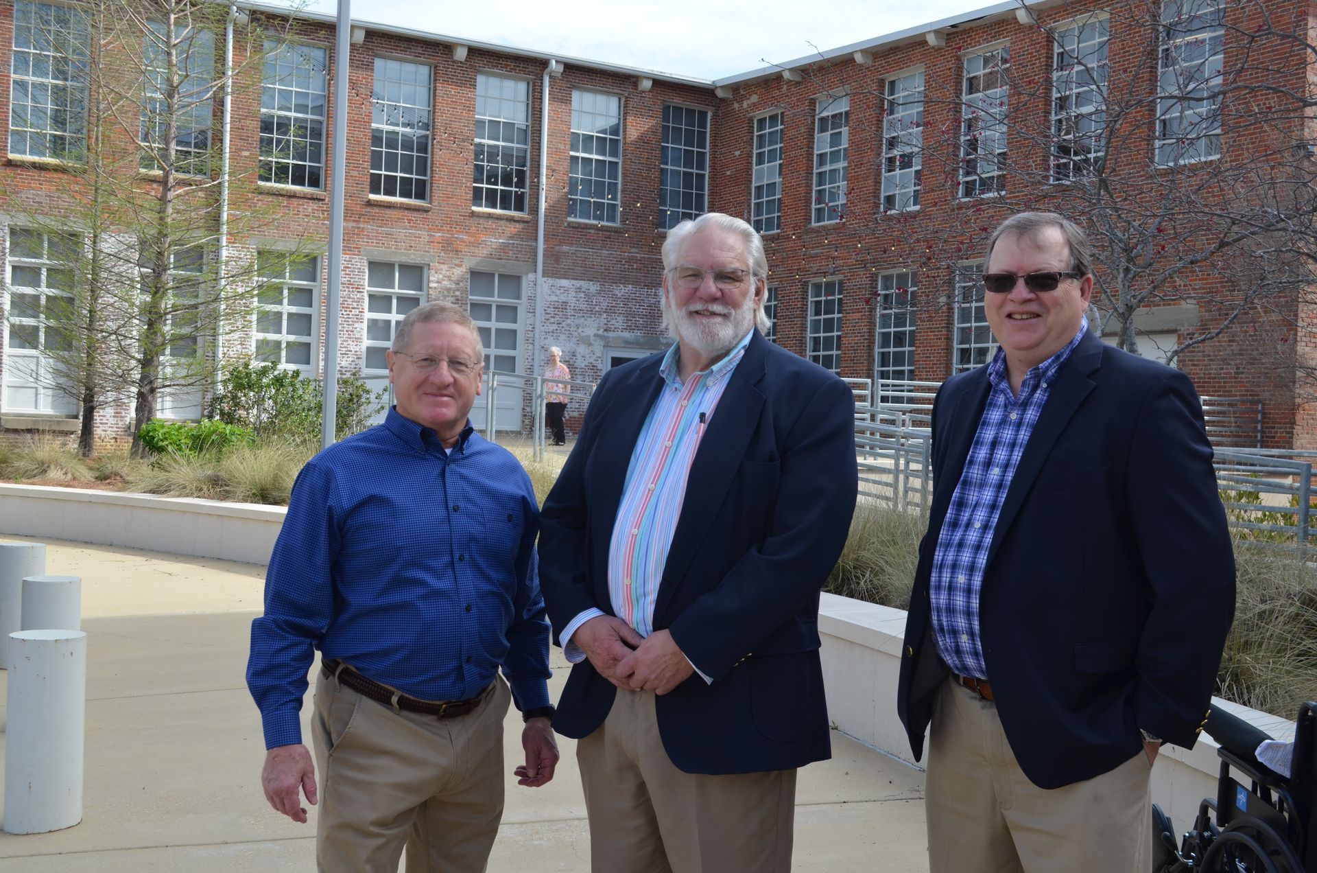 Three men are posing for a picture in front of a brick building.