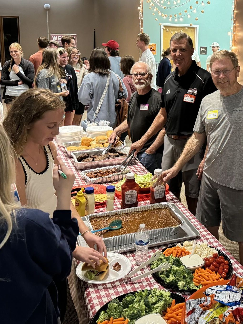 A group of people are standing around a table filled with food.