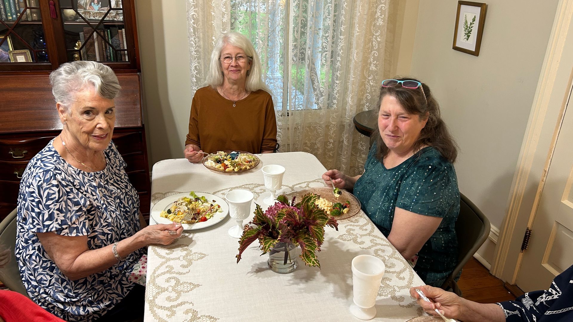 Three women at a table eating, a centerpiece in front, and a window behind them.