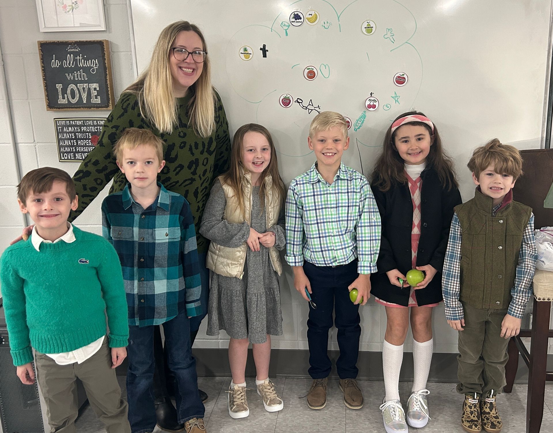 A group of children are posing for a picture with a teacher in a classroom.