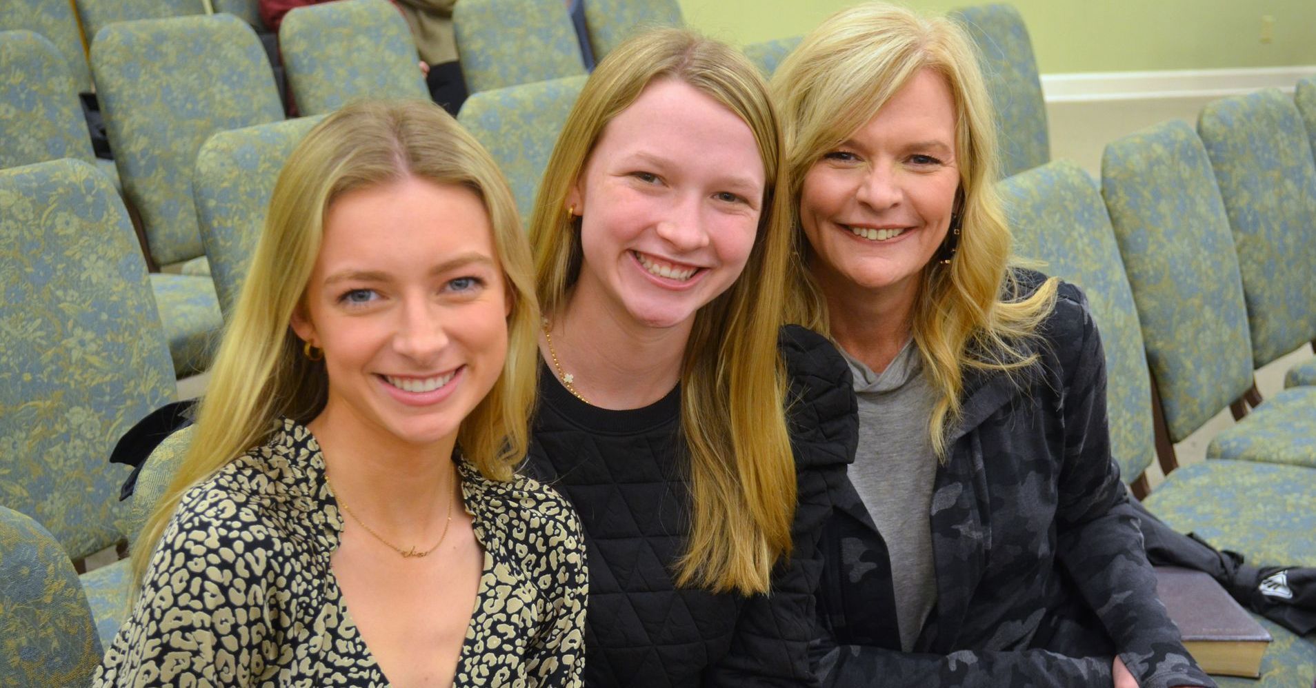 Three women are sitting in a row of chairs and smiling for the camera.