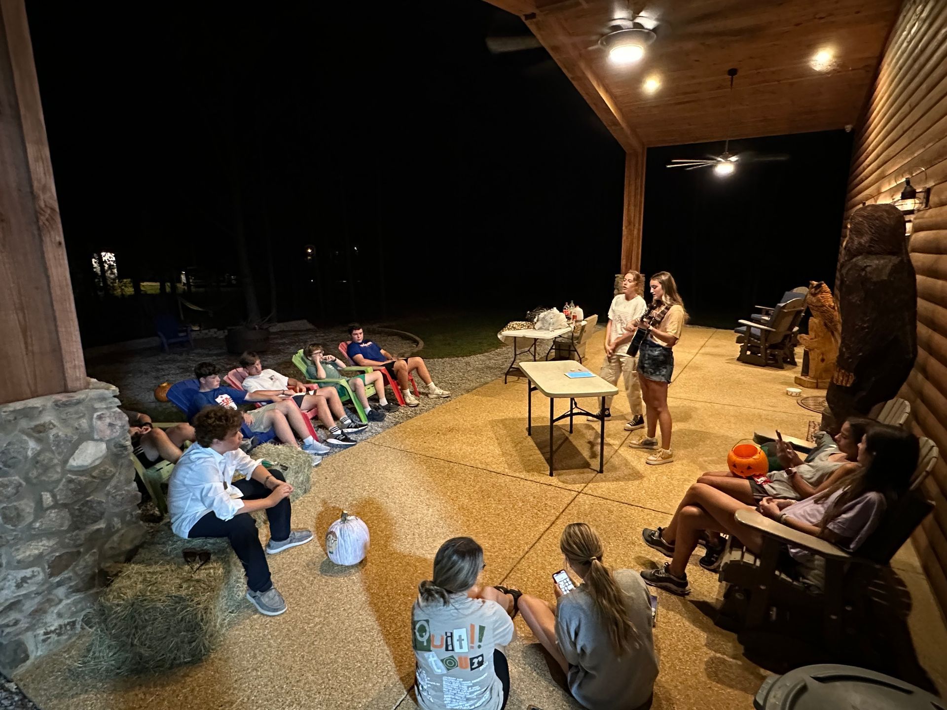 A group of people are sitting around a table on a porch at night.