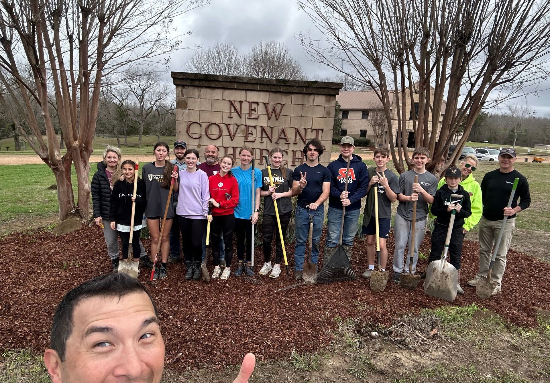 A group of people are standing in front of a sign holding shovels.