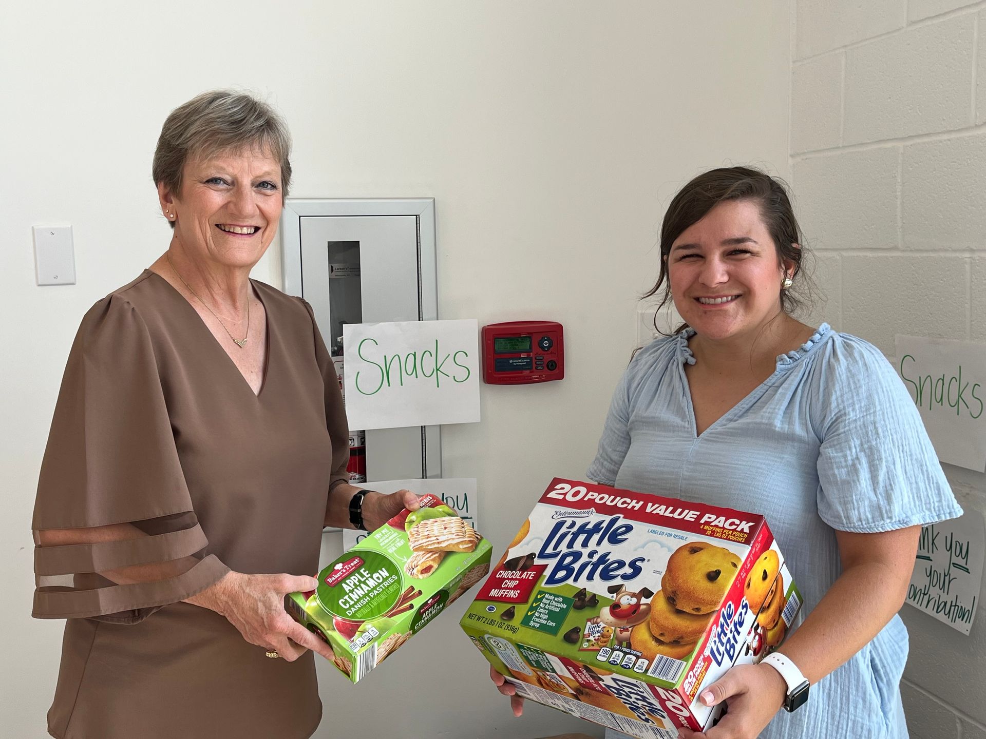 Two women are holding boxes of little bites cereal.