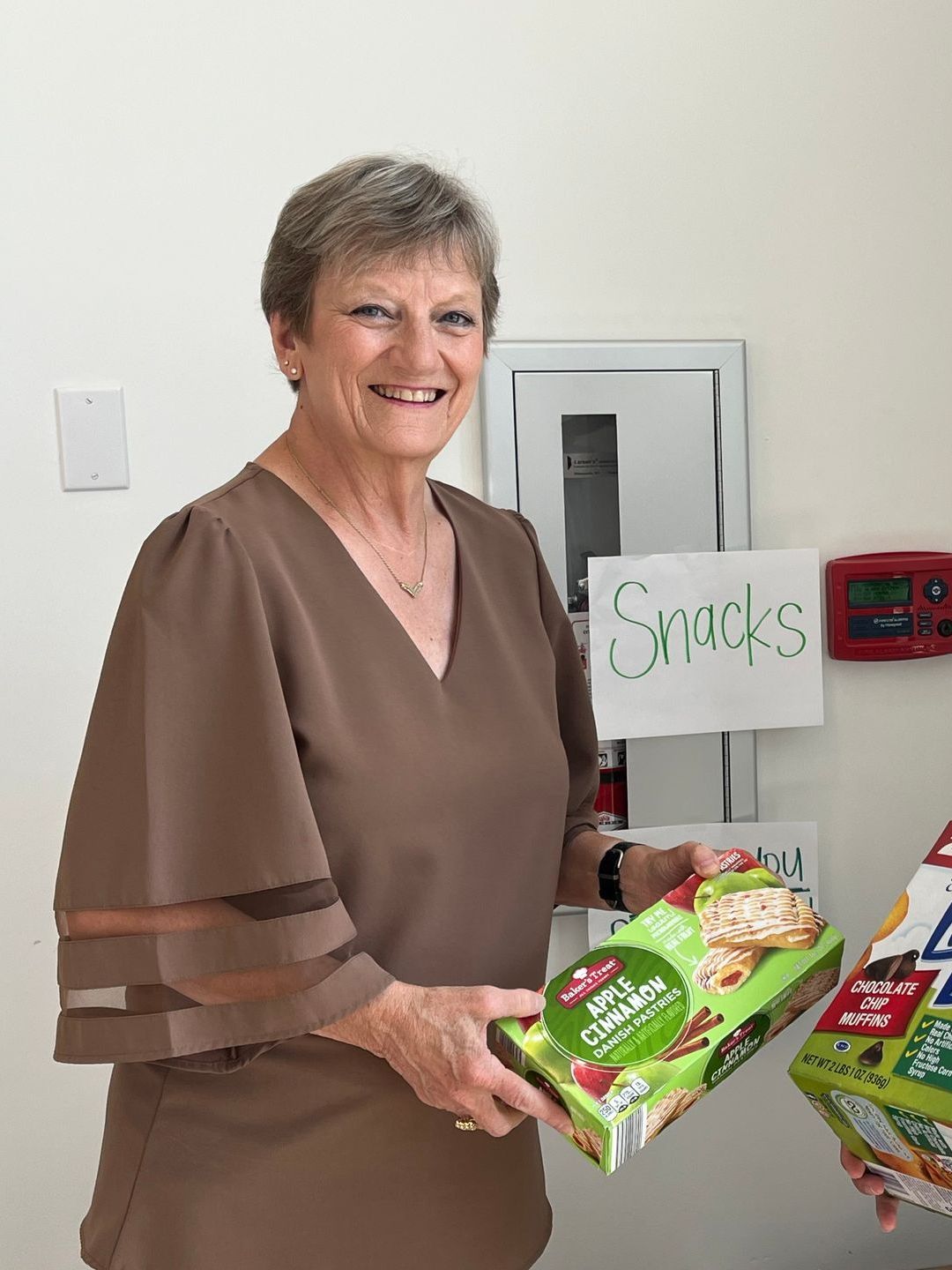 A woman is holding a box of snacks in front of a sign that says snacks.