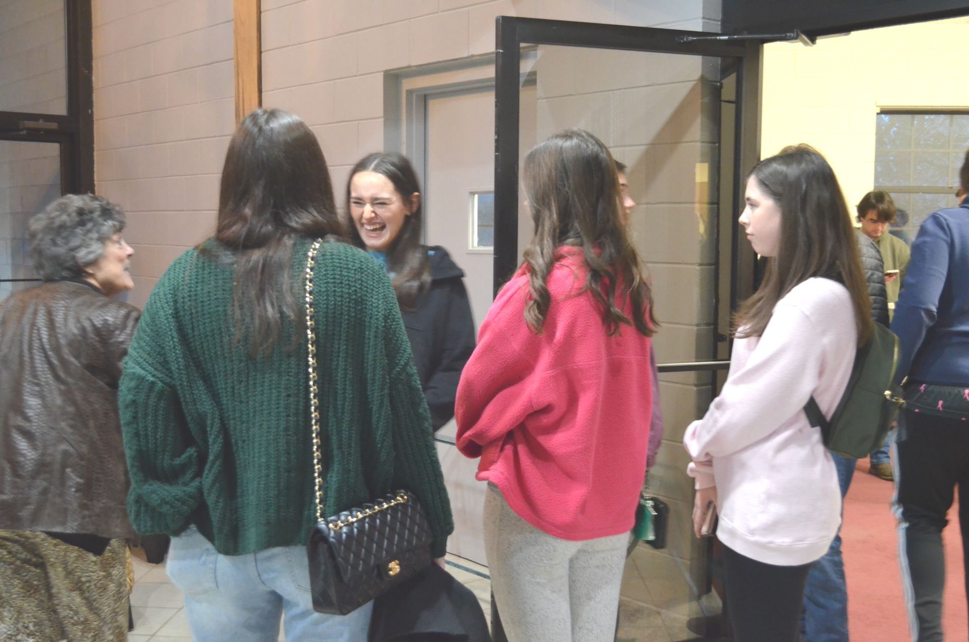 A group of young women are standing in a hallway talking to each other.