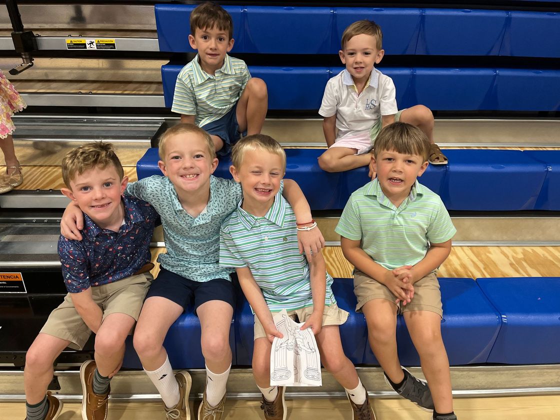 Group of boys sitting and smiling on blue bleachers; some have arms around each other.