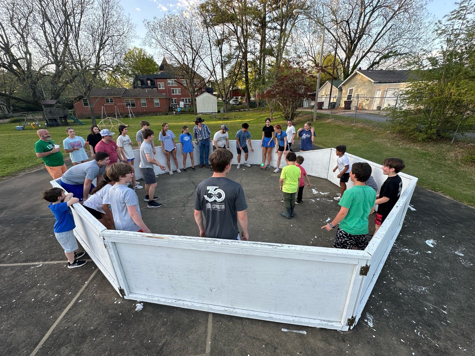 A group of people are standing around a white fence in a park.