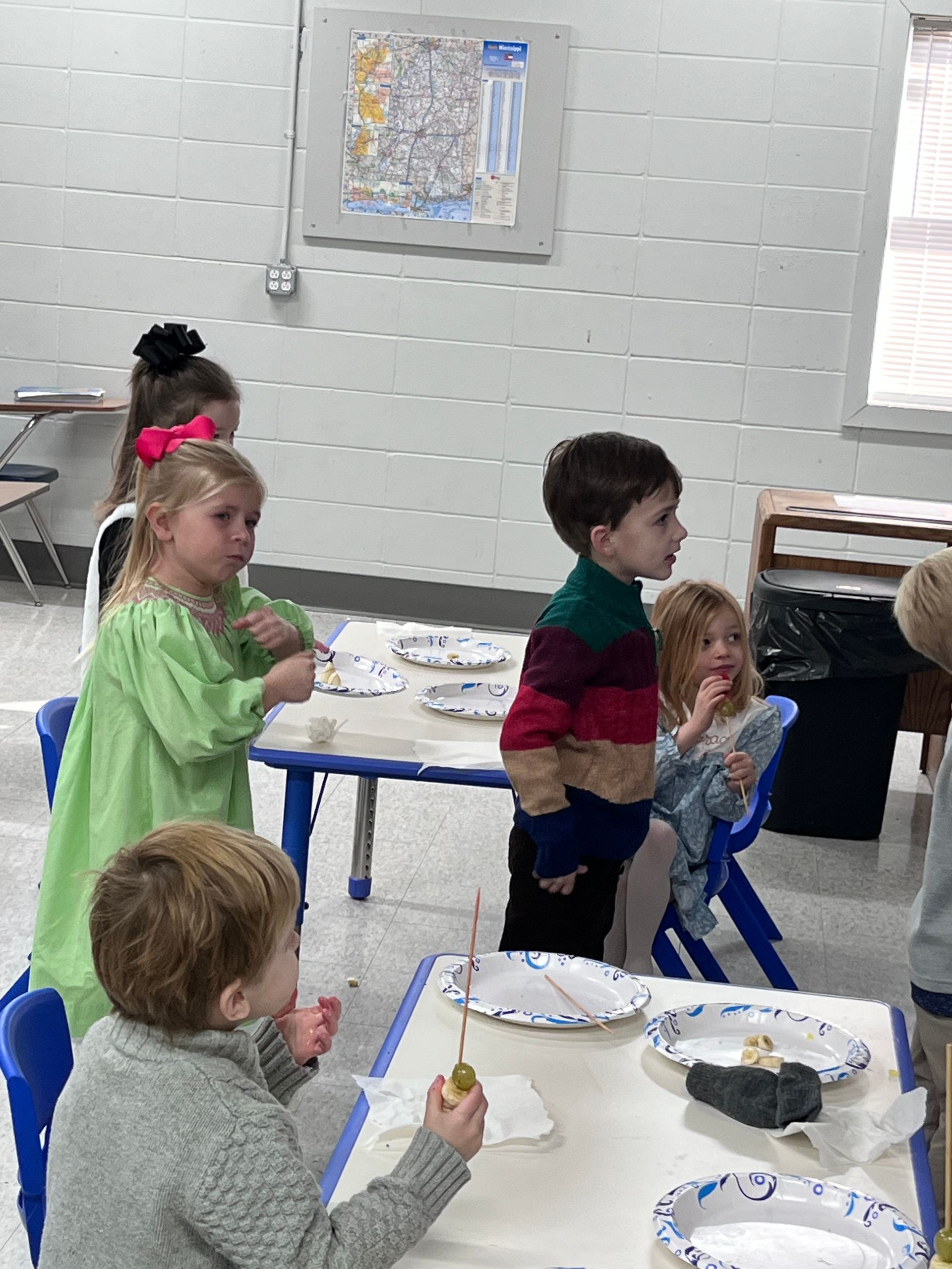A group of children are sitting at tables with plates of food.