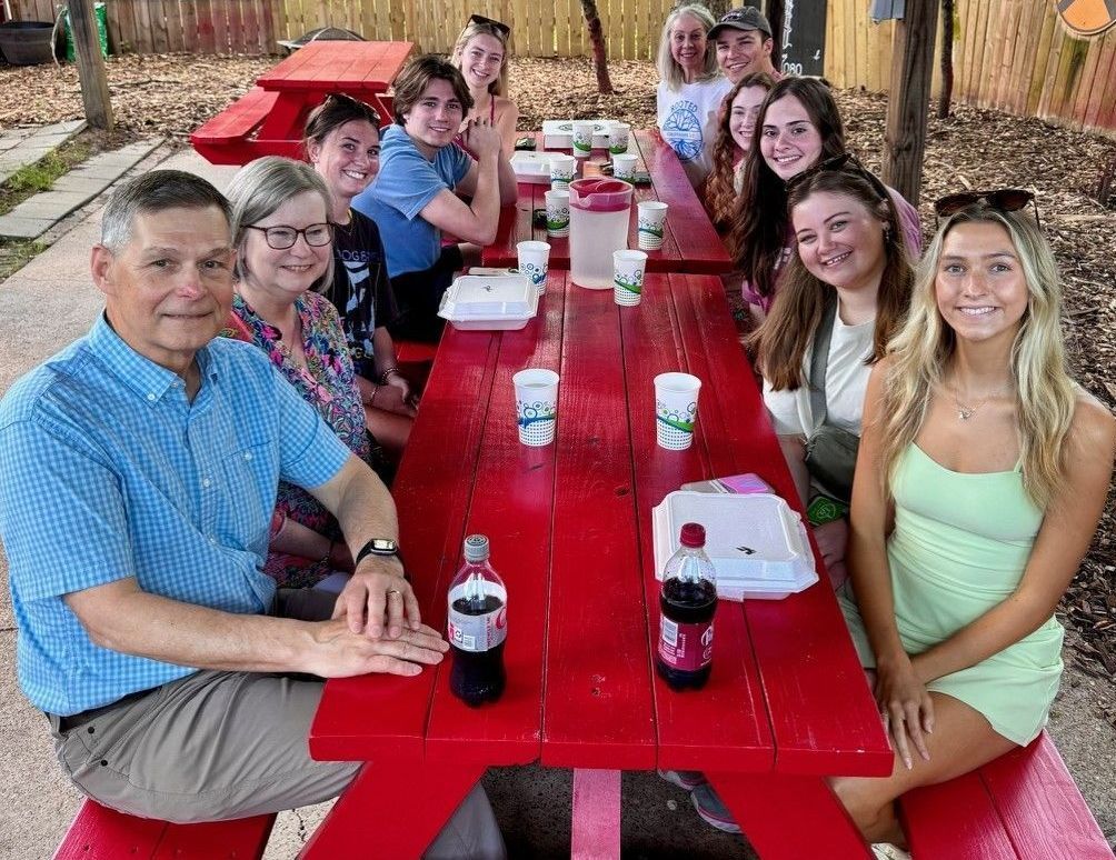 A group of people are sitting at a red picnic table.