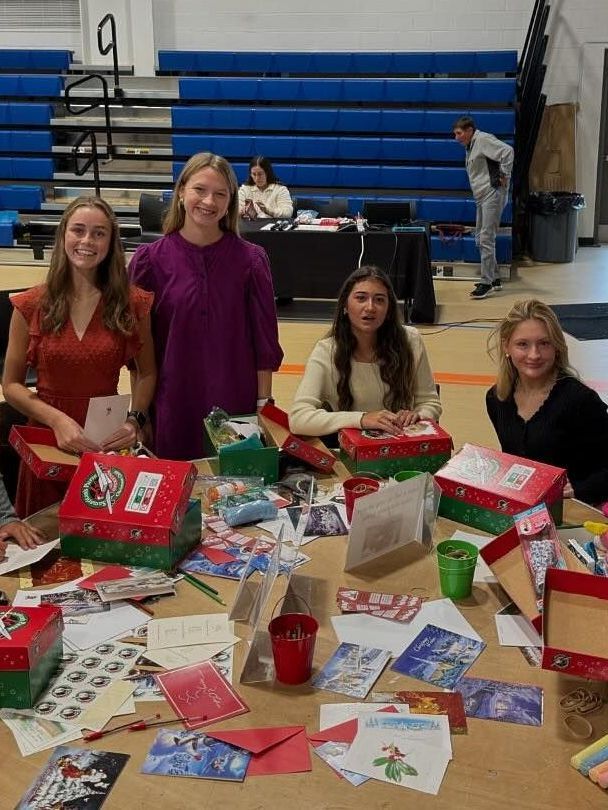 A group of young women are sitting at a table making christmas cards.