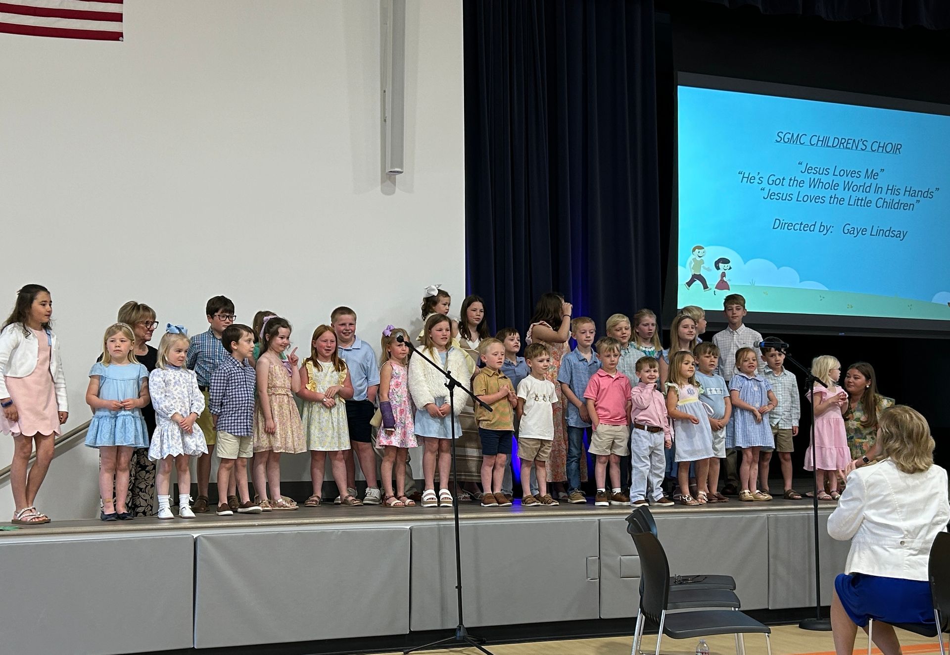 A group of children are standing on a stage singing into microphones.