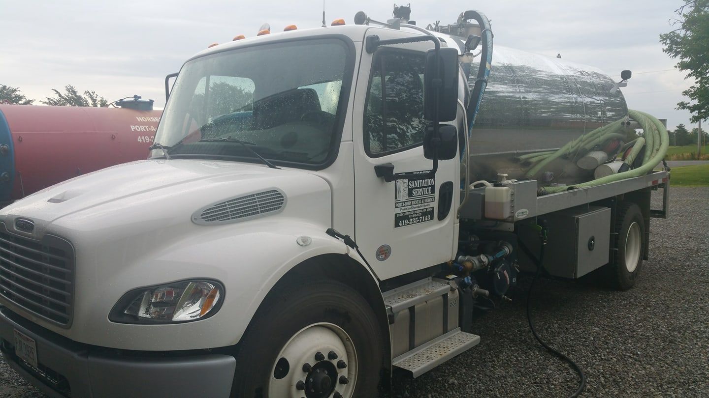 White Freightliner vacuum truck parked on a gravel lot with a chrome tank and green hoses.