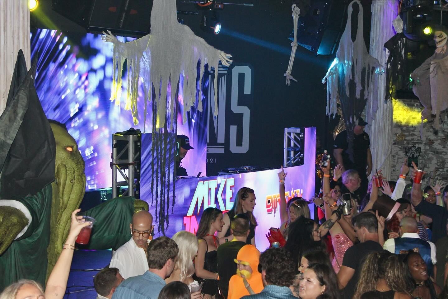 Crowd dancing under colorful stage lights at a nightclub or concert, with confetti and hanging decorations