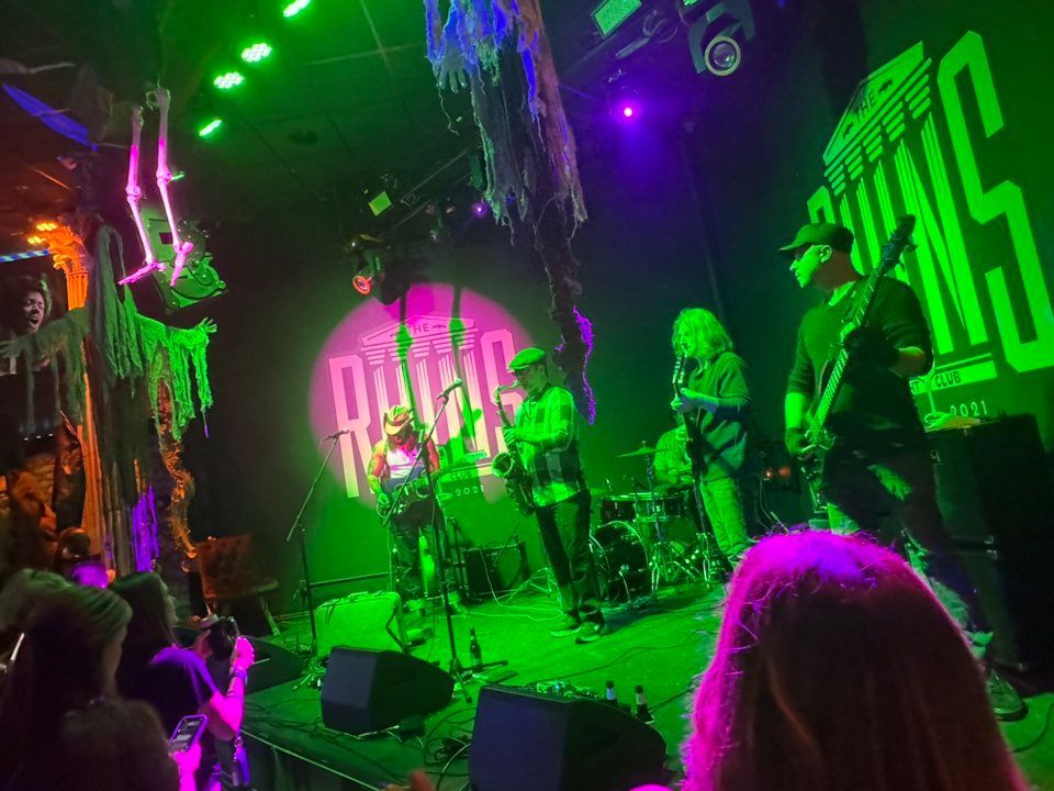 Live band performing on a neon green and purple-lit stage with audience watching in front