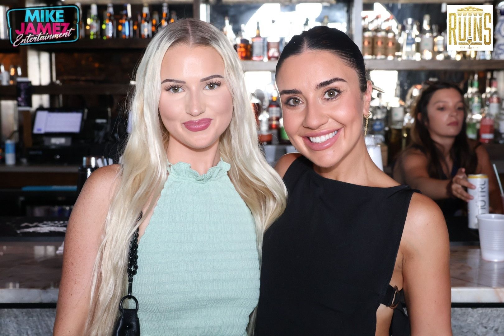 Two women posing together in a bar, smiling at the camera.