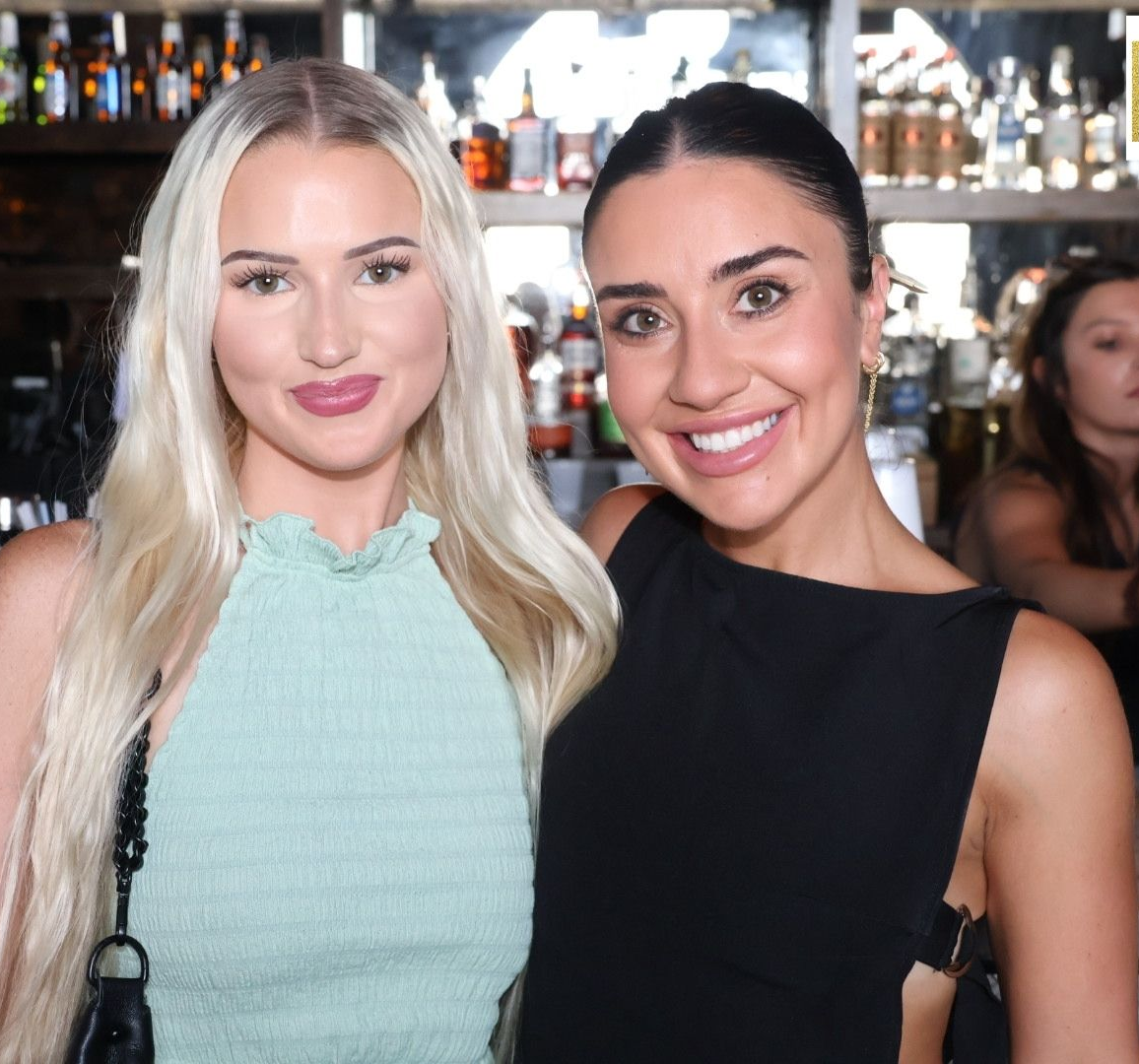 Two women smiling at a social event, one in a mint dress and one in a black sleeveless top.