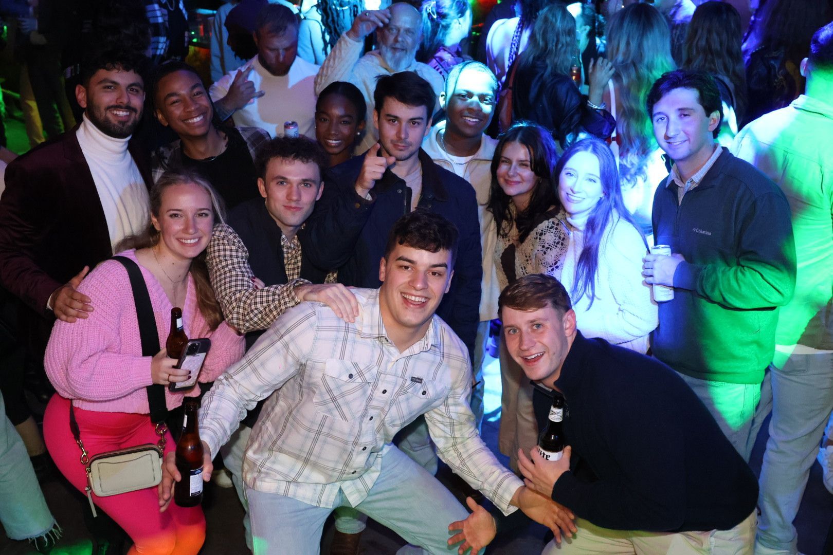 Group of people posing together at a lively party, smiling under colorful blue and green lights.
