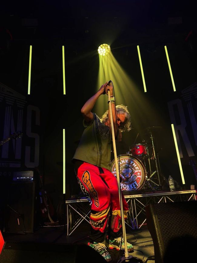 Singer in red pants performing on stage under yellow lights, singing into a microphone stand.