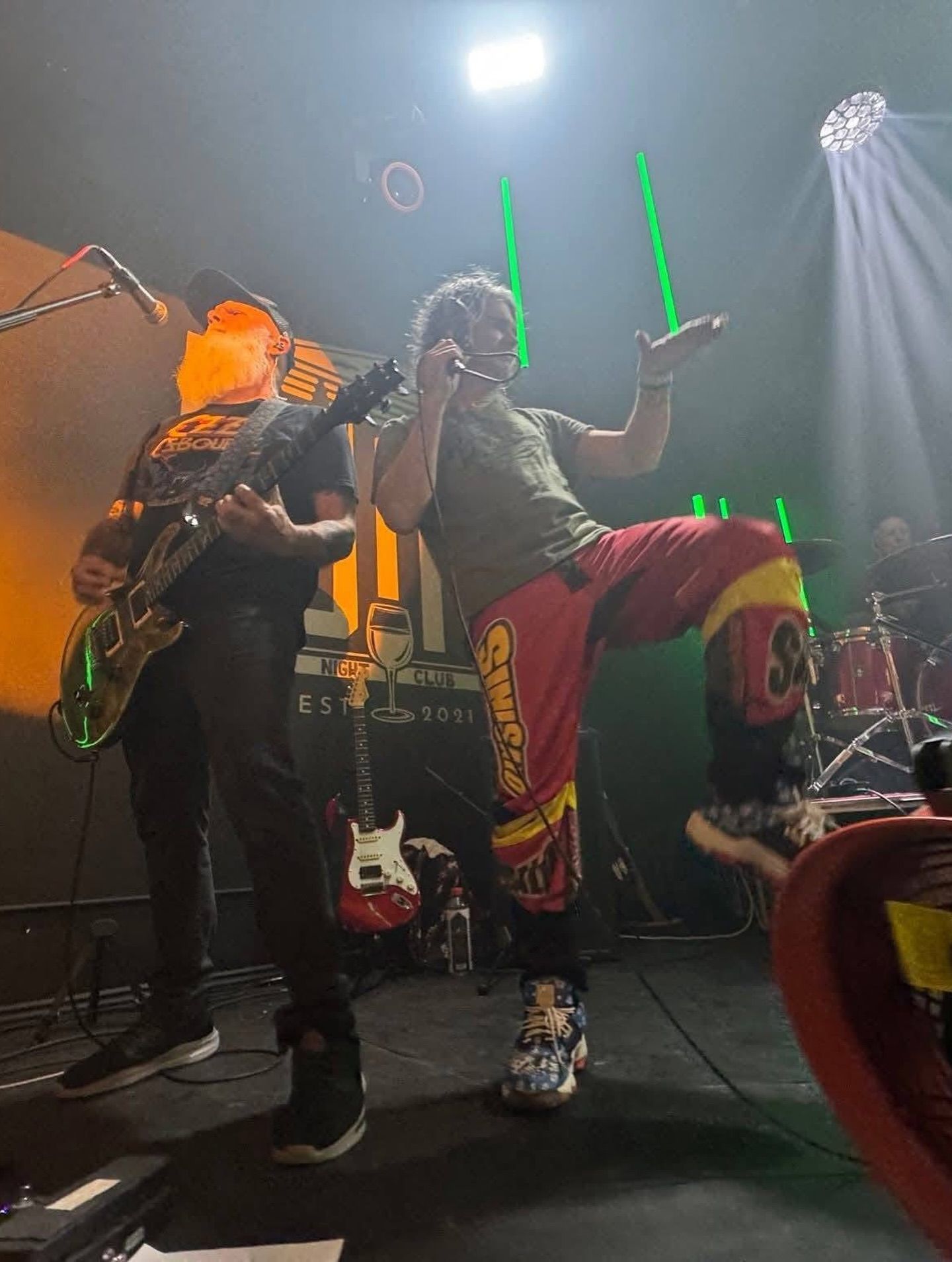 Rock band performing live onstage with electric guitars, colorful lighting, and raised hands in the crowd