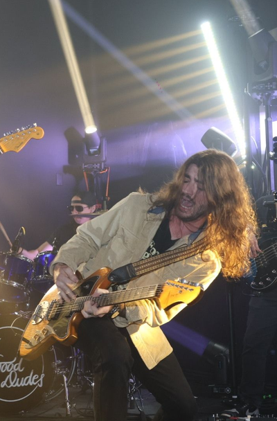 Guitarist leaning back onstage under bright stage lights, playing a gold electric guitar.