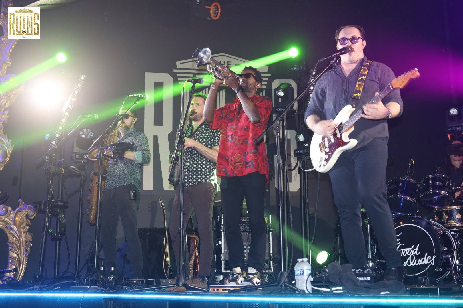 Live band performing on stage with green lights and microphones