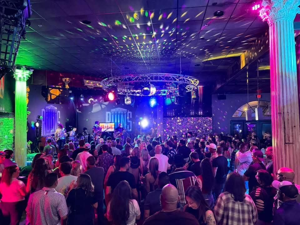 Crowded nightclub dance floor with colorful stage lights and a cheering crowd