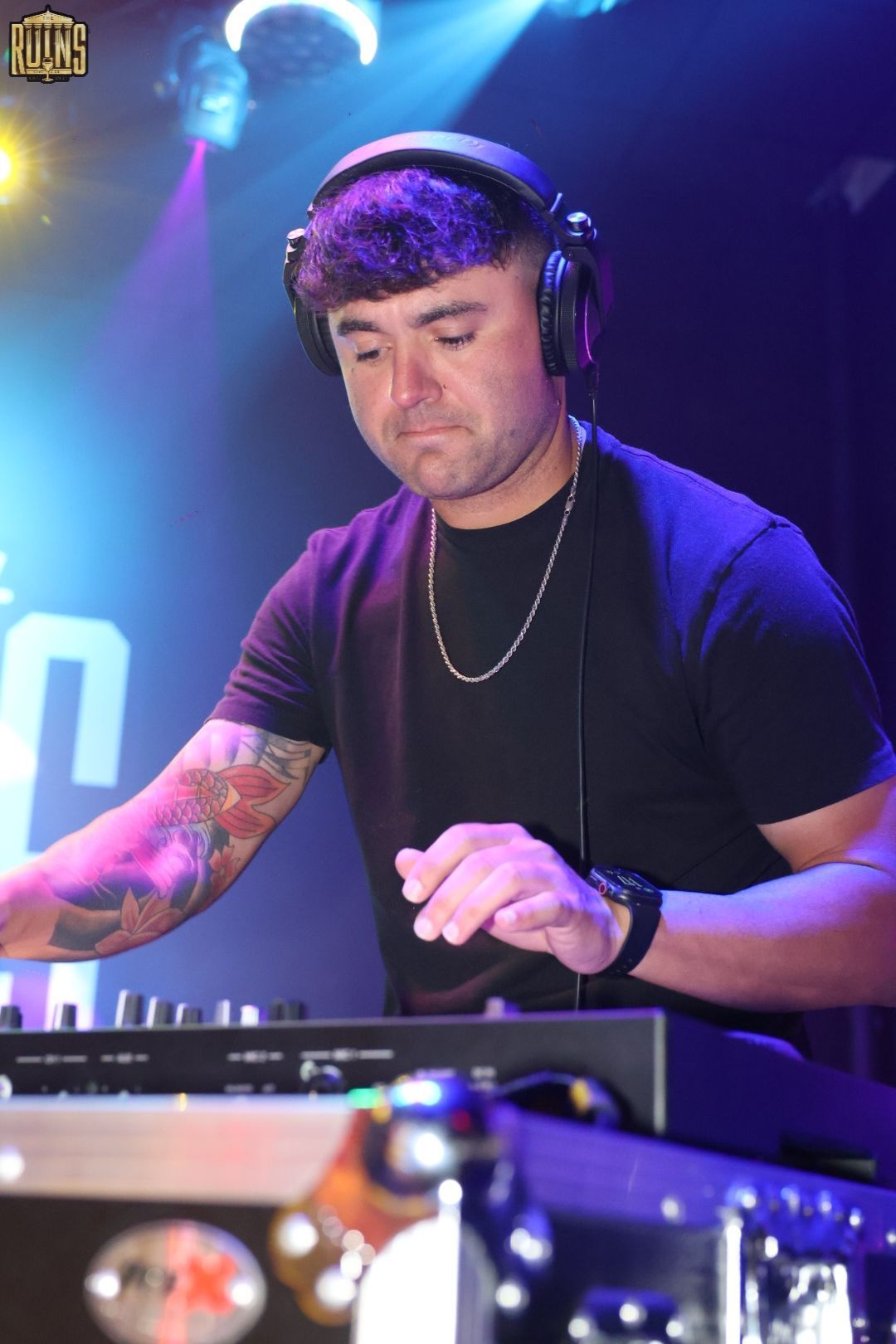 DJ wearing headphones and black shirt mixing music under purple and blue club lights