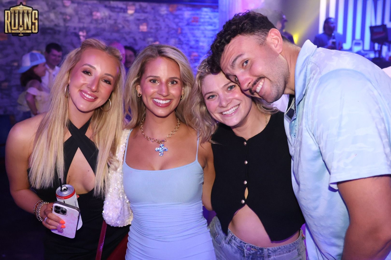 Four friends smiling and posing at a nightclub, with purple lighting in the background.