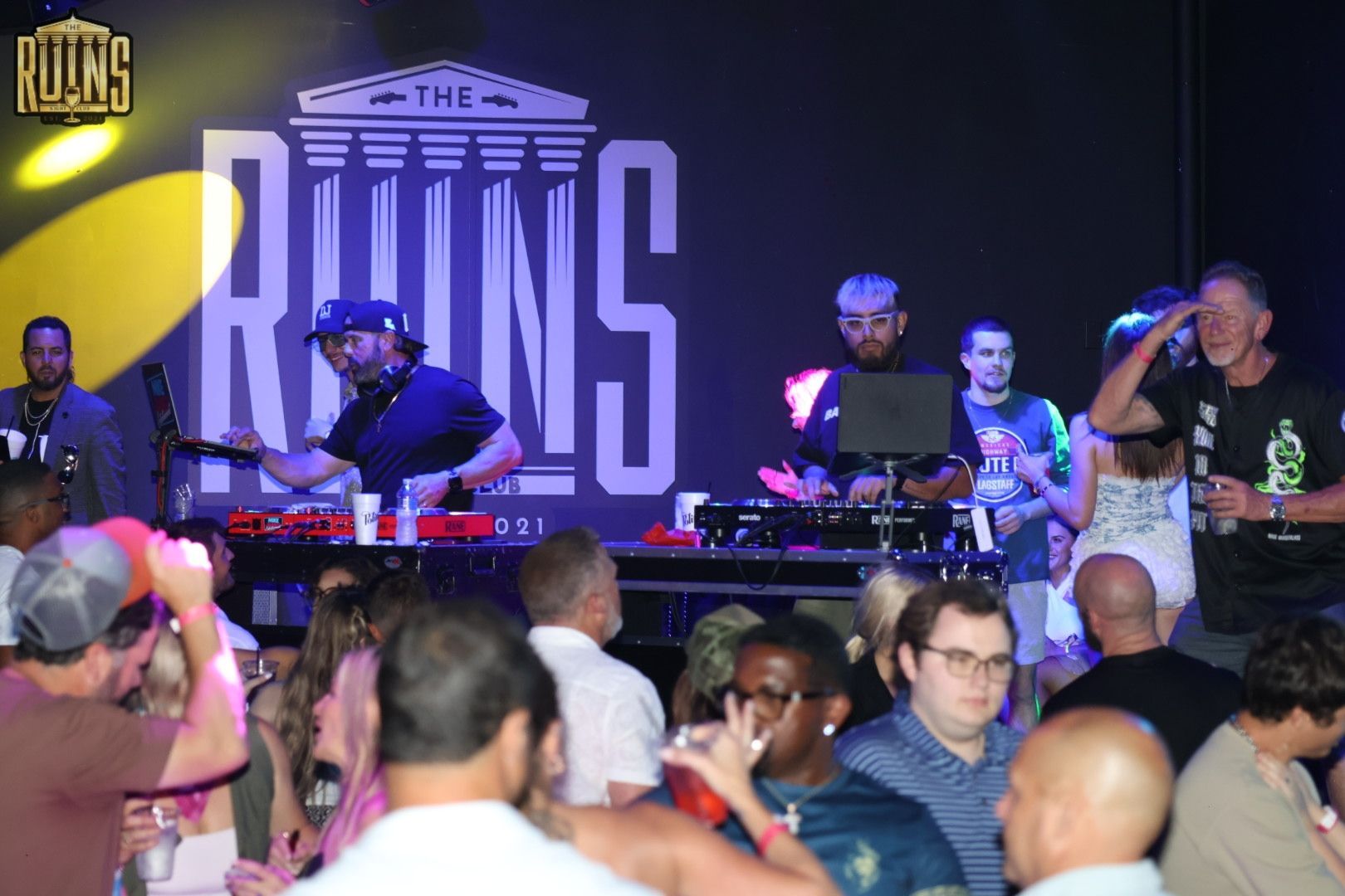DJ crew performing onstage at The Ruins, with a crowd dancing in the foreground