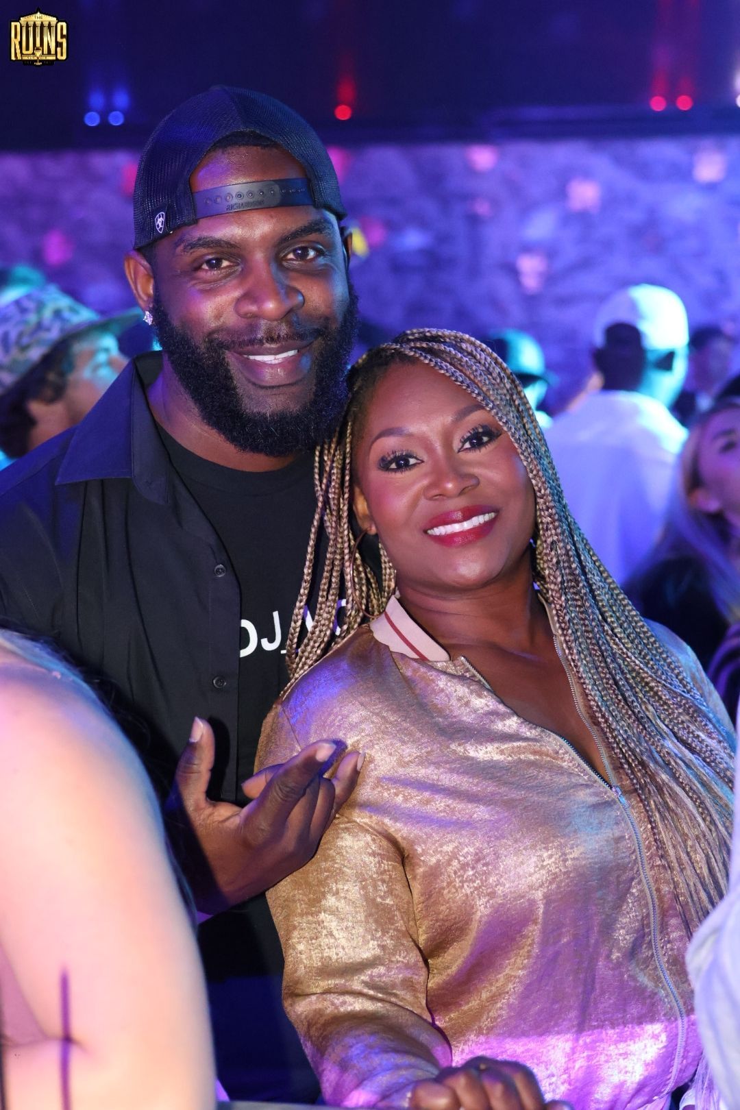 Two smiling people posing together in a dimly lit club with purple lighting