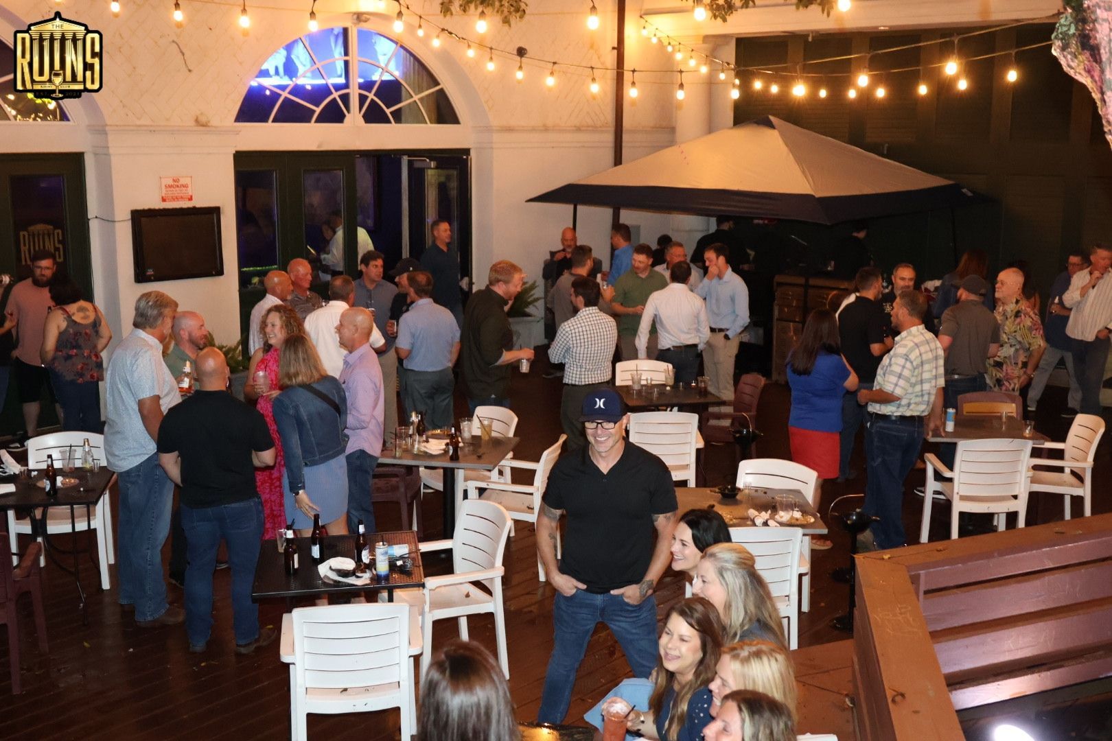 Crowded patio party with people mingling under string lights and umbrellas at night