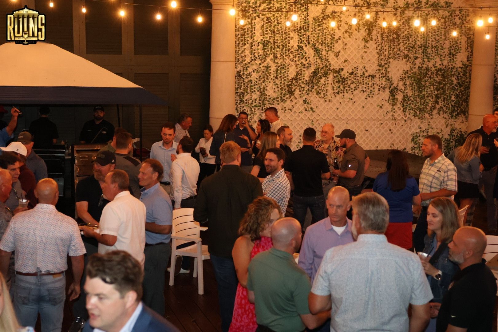 People mingling at a crowded evening outdoor event under string lights and umbrellas