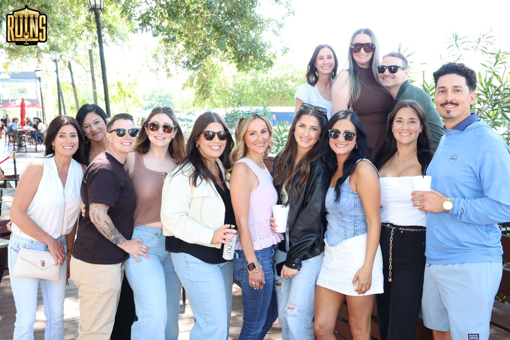 Group of people posing outdoors in sunglasses, smiling together in a sunny park.