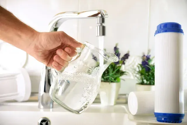 A person is pouring water into a glass from a faucet in Vancouver, WA