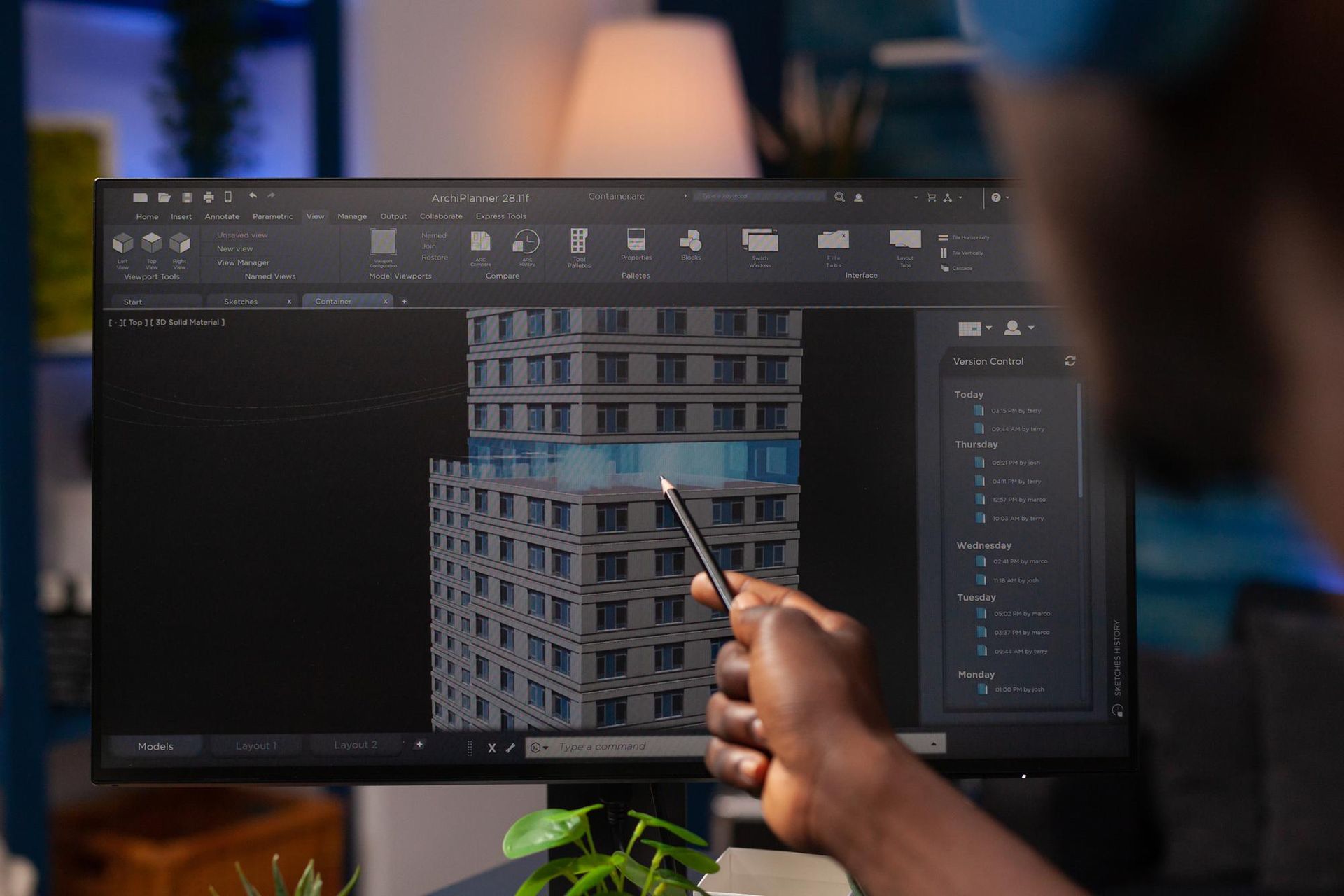 Architect using a pen to point at a 3D model of a building on a computer screen.